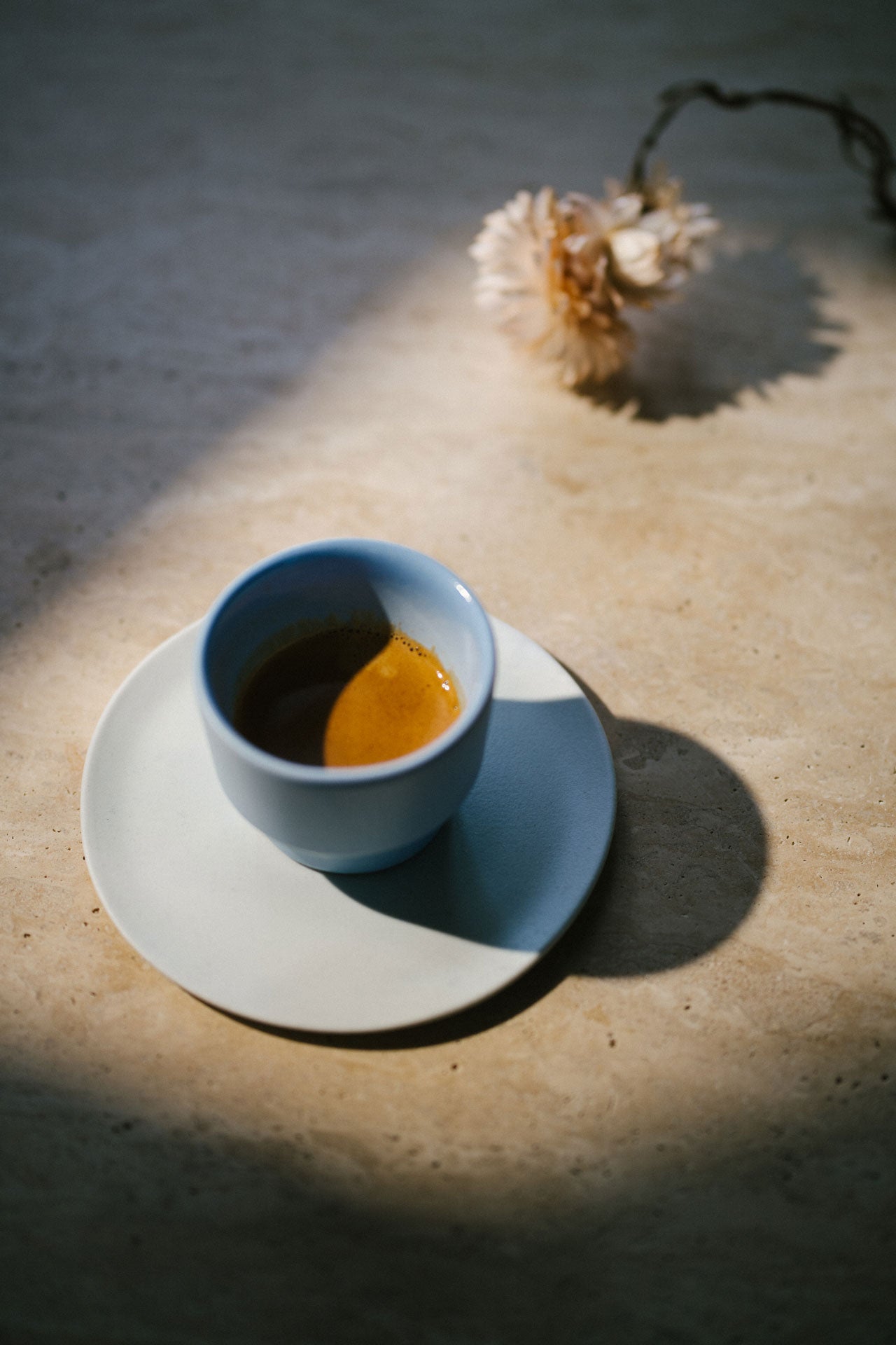 Espresso in einer hellblauen Espressotasse mit einer Trockenblume daneben