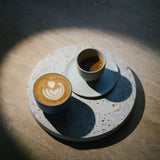 Ein Cappuccino steht neben einem Espresso auf einer Steinplatte im Tarazzo-Muster