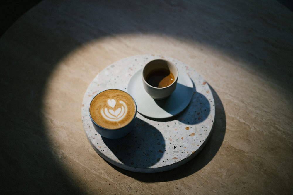 Ein Cappuccino steht neben einem Espresso auf einer Steinplatte im Tarazzo-Muster