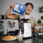 Eine Frau schüttet den Kaffee PRIMO in die Espressomühle in einer Küche