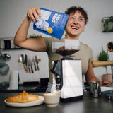 Eine Frau schüttet den Kaffee PRIMO in die Espressomühle in einer Küche